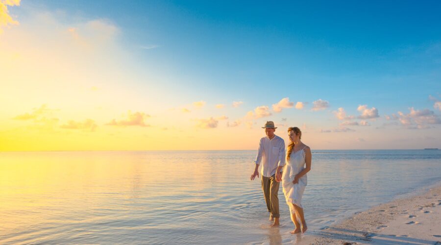 couple walking on seashore wearing white tops during sunset